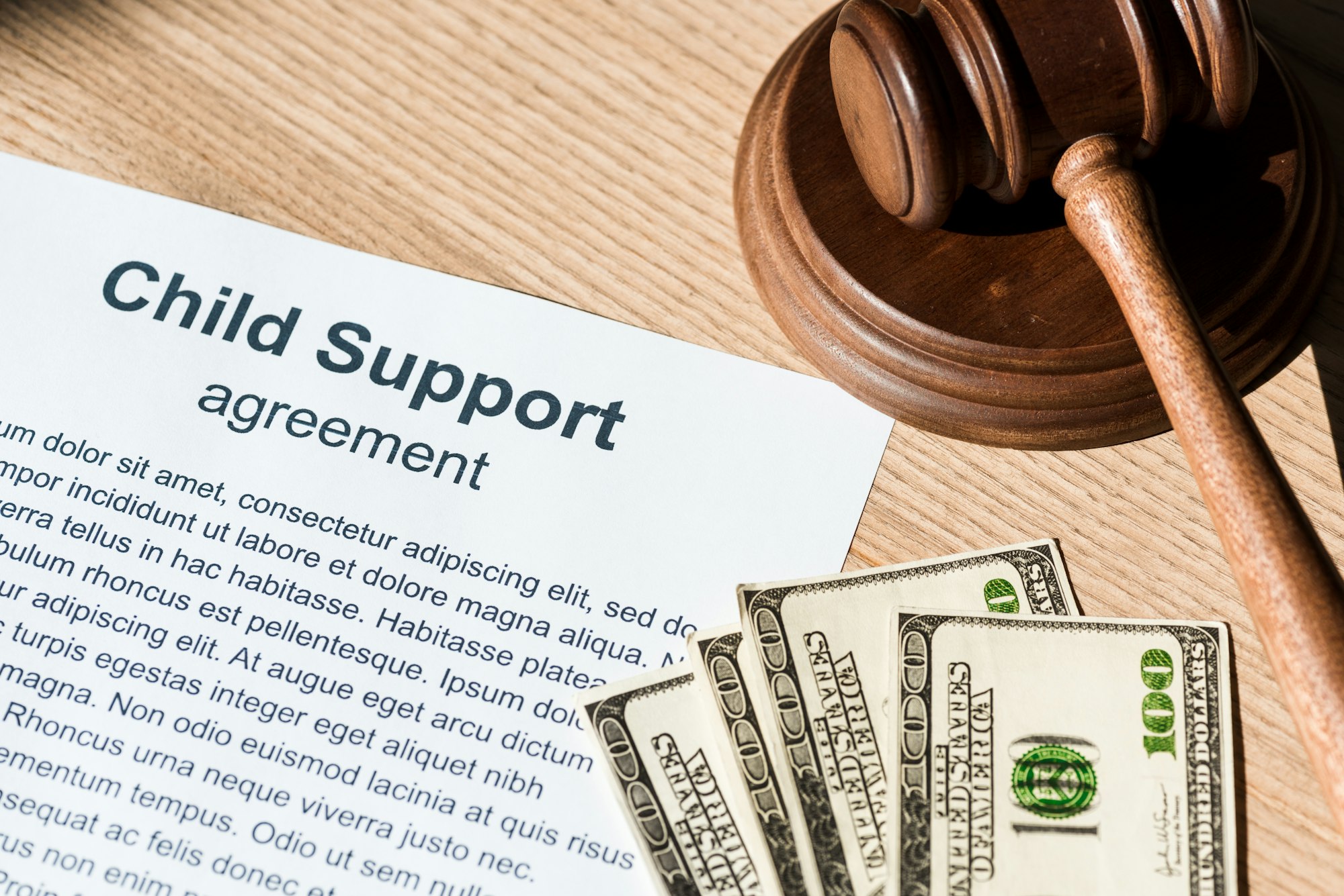 wooden gavel near document with child support agreement and dollar banknotes