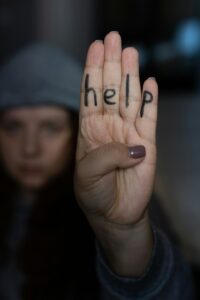 Young woman wearing gray hat showing four fingers with inscription on hand saying help. Sign of